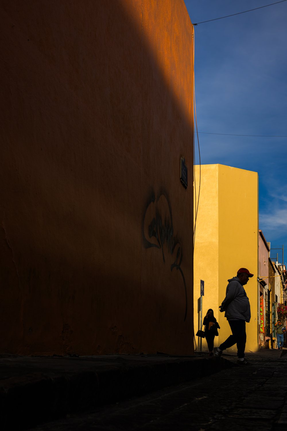 Street photography: a passerby in silhouette beside a sunlit yellow house, in WorthWait's Positive film