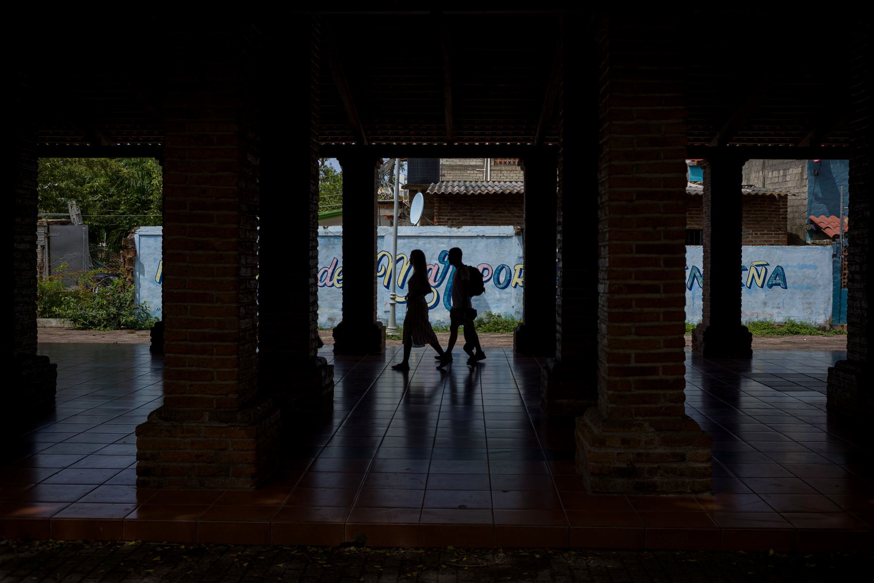 Fixed 35mm lens street photography: two figures in silhouette walk past the columns of a shaded arcade