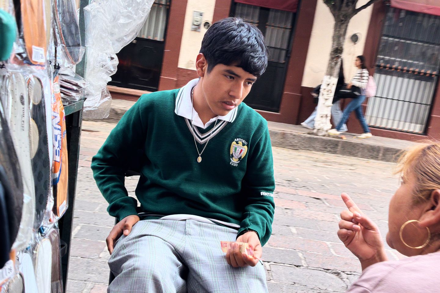 Street photography app: a schoolboy in a green sweater listens to a woman on a cobblestone sidewalk, Negative film